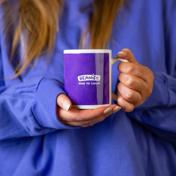 Blue branded Beanies Cup/mug held by a woman wearing a blue hoodie. Her face is cropped out the photo.