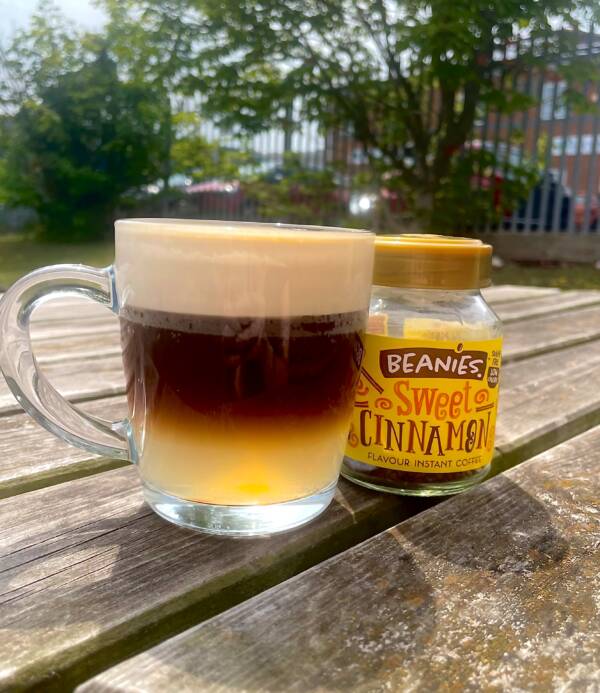 Ginger Rush Coffee in glass mug. 3 layers of ginger beer, sweet cinnamon coffee and double cream can be seen. A jar of Beanies Sweet Cinnamon Coffee is to the right of the drink.